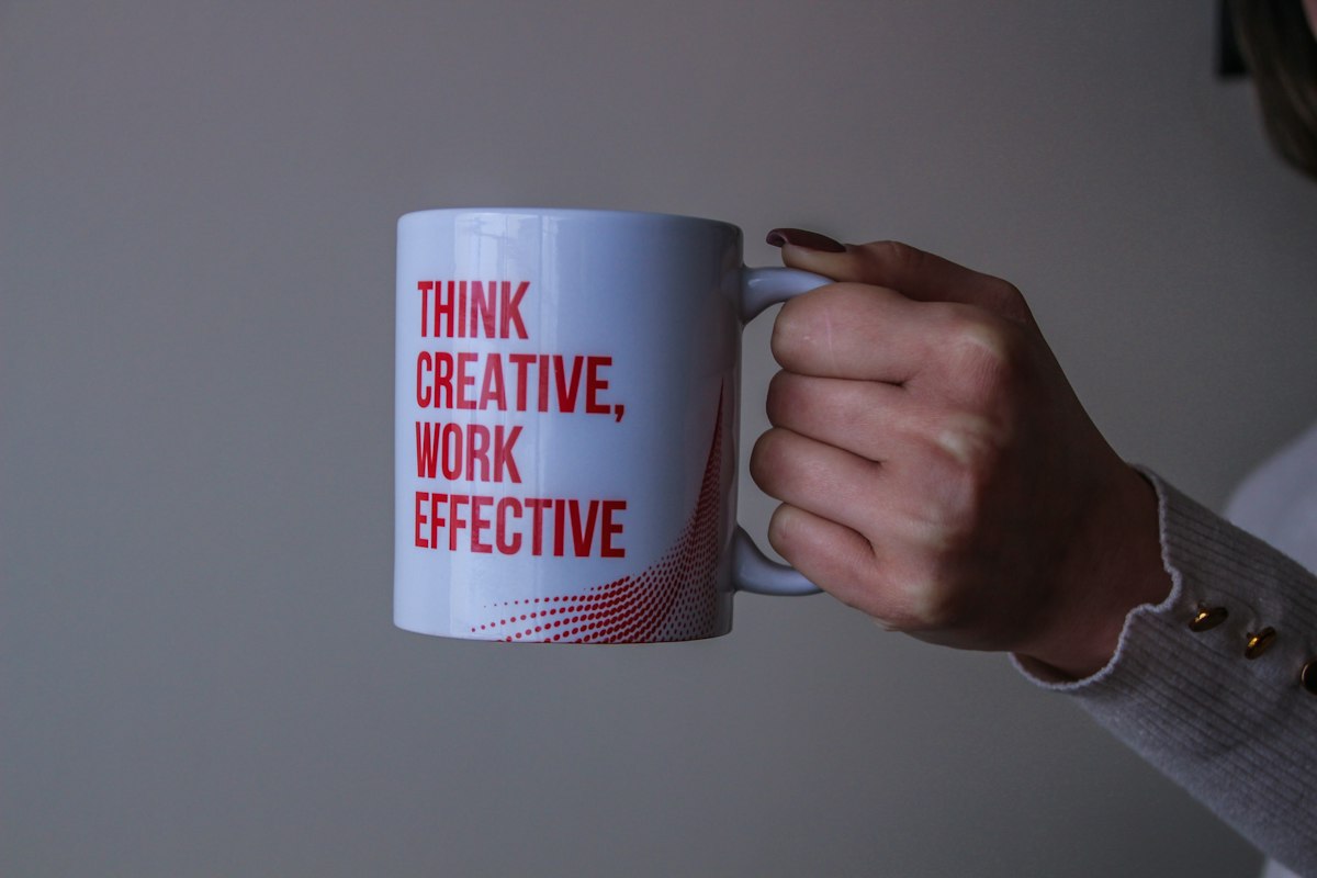 Hand holding a mug that reads Think creative, work effective